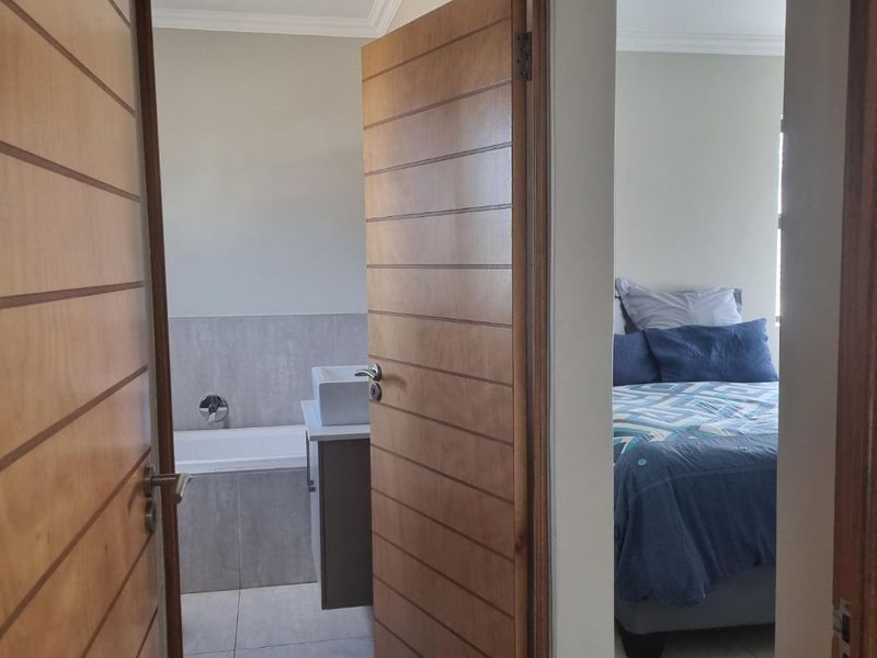 A view from the hallway looking into a bathroom with a built-in vanity and bathtub, and a bedroom with tiled flooring.