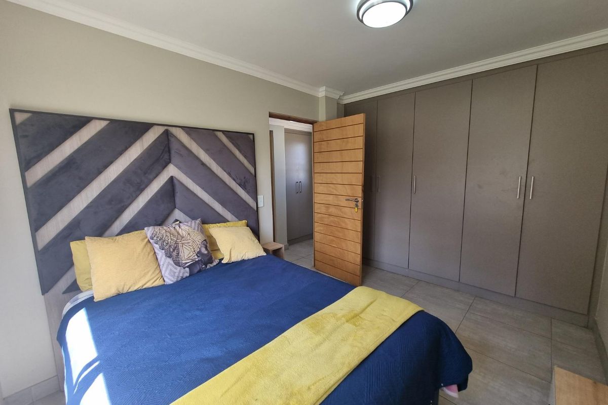 A well-maintained bedroom featuring neutral tiled flooring, extensive built-in cupboards, and a modern ceiling light fixture.