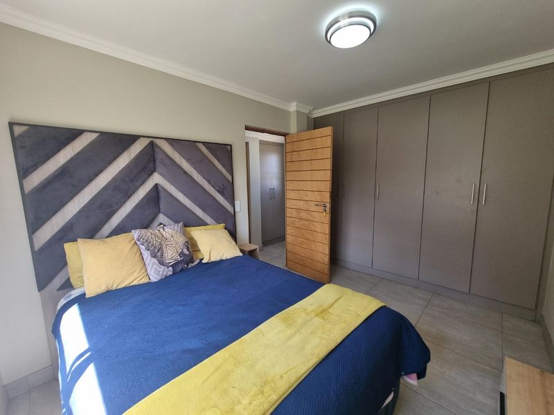 A well-maintained bedroom featuring neutral tiled flooring, extensive built-in cupboards, and a modern ceiling light fixture.