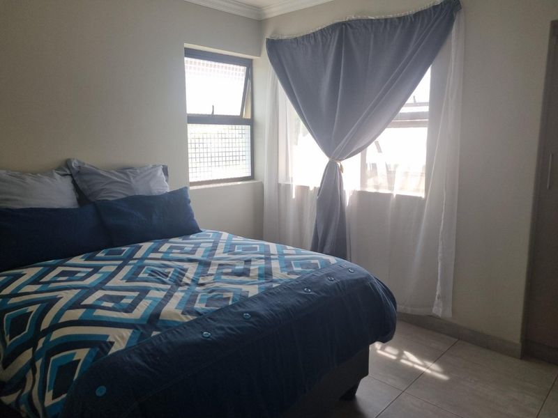 A functional bedroom featuring tiled flooring, built-in storage, and natural light through casement windows.