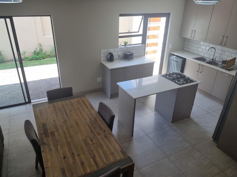 Modern open-plan kitchen and dining area featuring a central island with gas hob, sleek cabinetry, subway tile backsplash, and direct access to the patio.