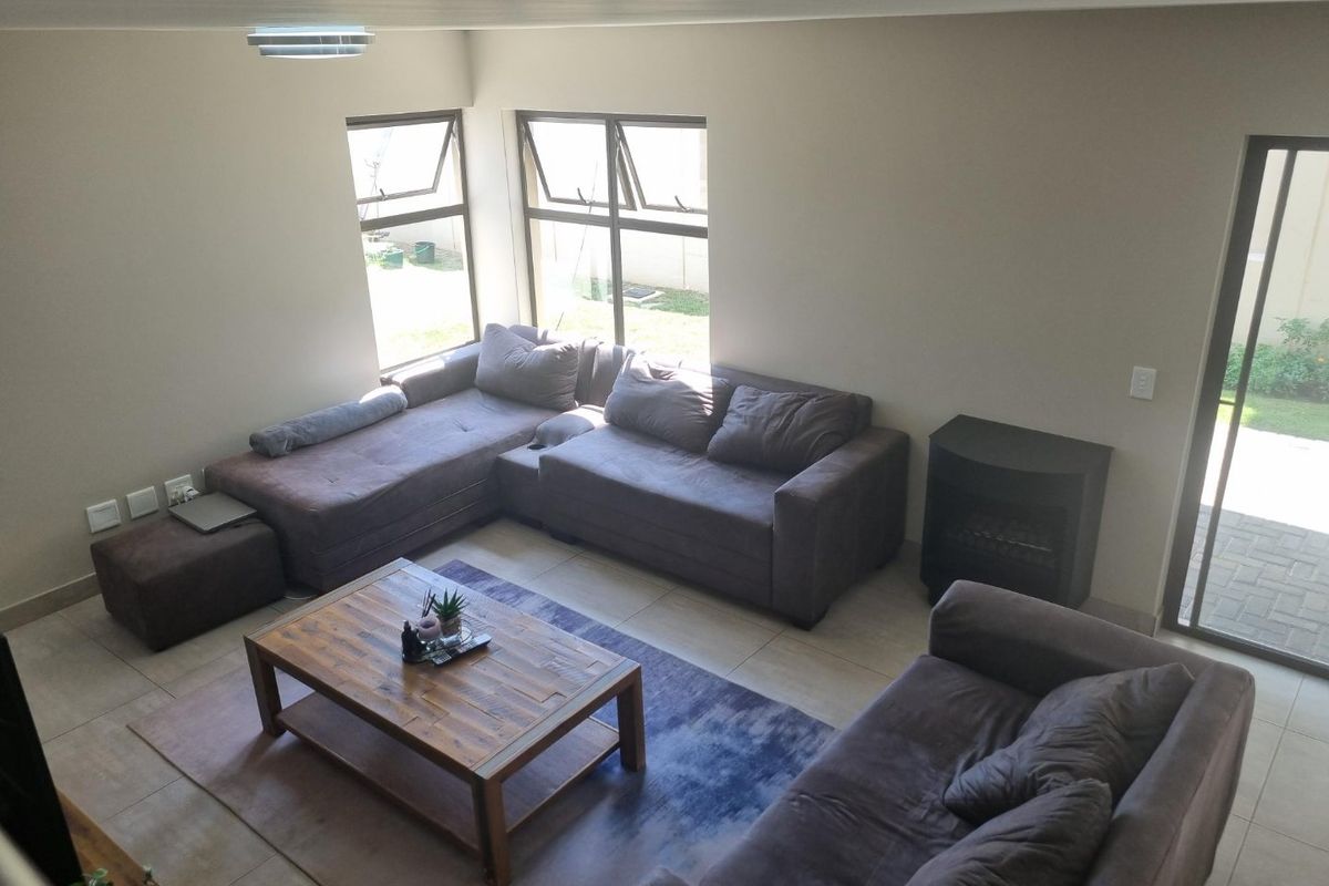 Spacious living room featuring tiled flooring, large windows for natural light, and a built-in fireplace with direct access to the outdoor area.