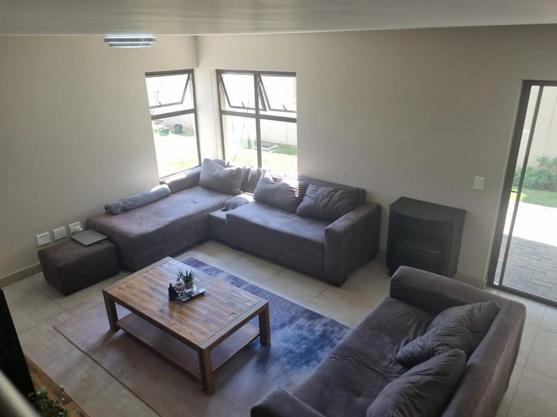 Spacious living room featuring tiled flooring, large windows for natural light, and a built-in fireplace with direct access to the outdoor area.