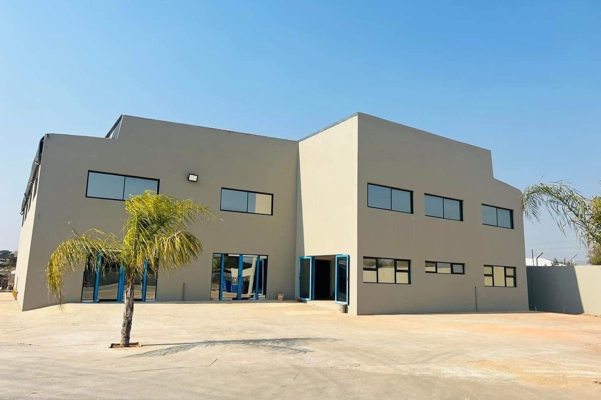 A modern commercial building exterior featuring a large concrete paved yard, clean rendered facade, and multiple aluminium-framed windows and doors.