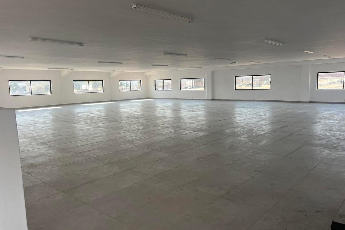A spacious, open-plan commercial interior featuring tiled flooring, ample natural light from multiple windows, and overhead fluorescent lighting.