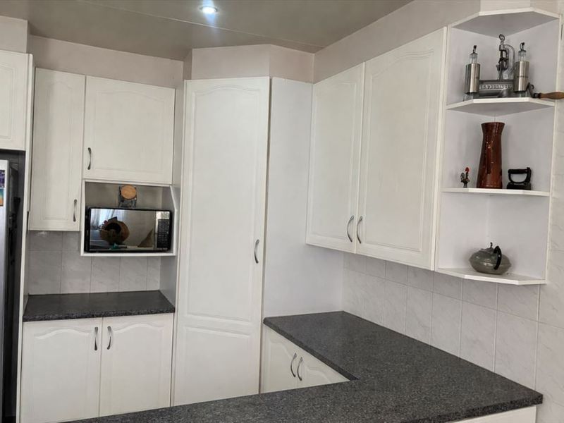A functional kitchen featuring white built-in cabinetry, dark granite countertops, and a tiled backsplash with integrated storage shelving.