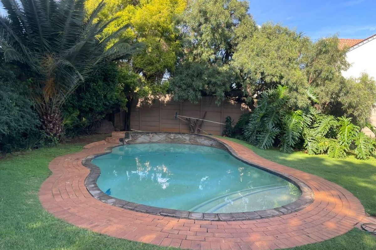 A private backyard featuring a swimming pool with brick coping, surrounded by established trees and a boundary wall.