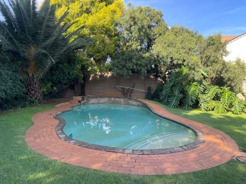 A private backyard featuring a swimming pool with brick coping, surrounded by established trees and a boundary wall.