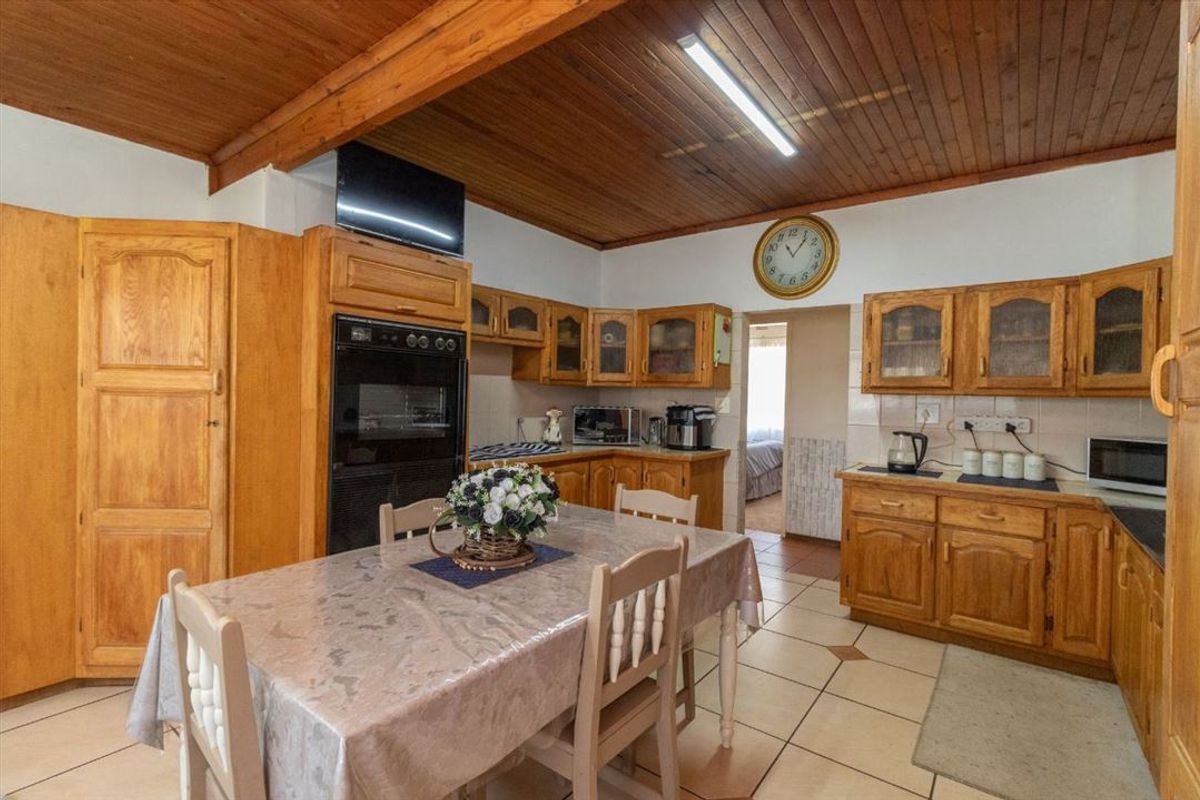 A traditional kitchen featuring extensive wooden cabinetry, a timber-clad ceiling, and tiled flooring, offering a functional layout with integrated oven and ample storage space.