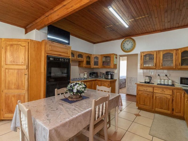 A traditional kitchen featuring extensive wooden cabinetry, a timber-clad ceiling, and tiled flooring, offering a functional layout with integrated oven and ample storage space.