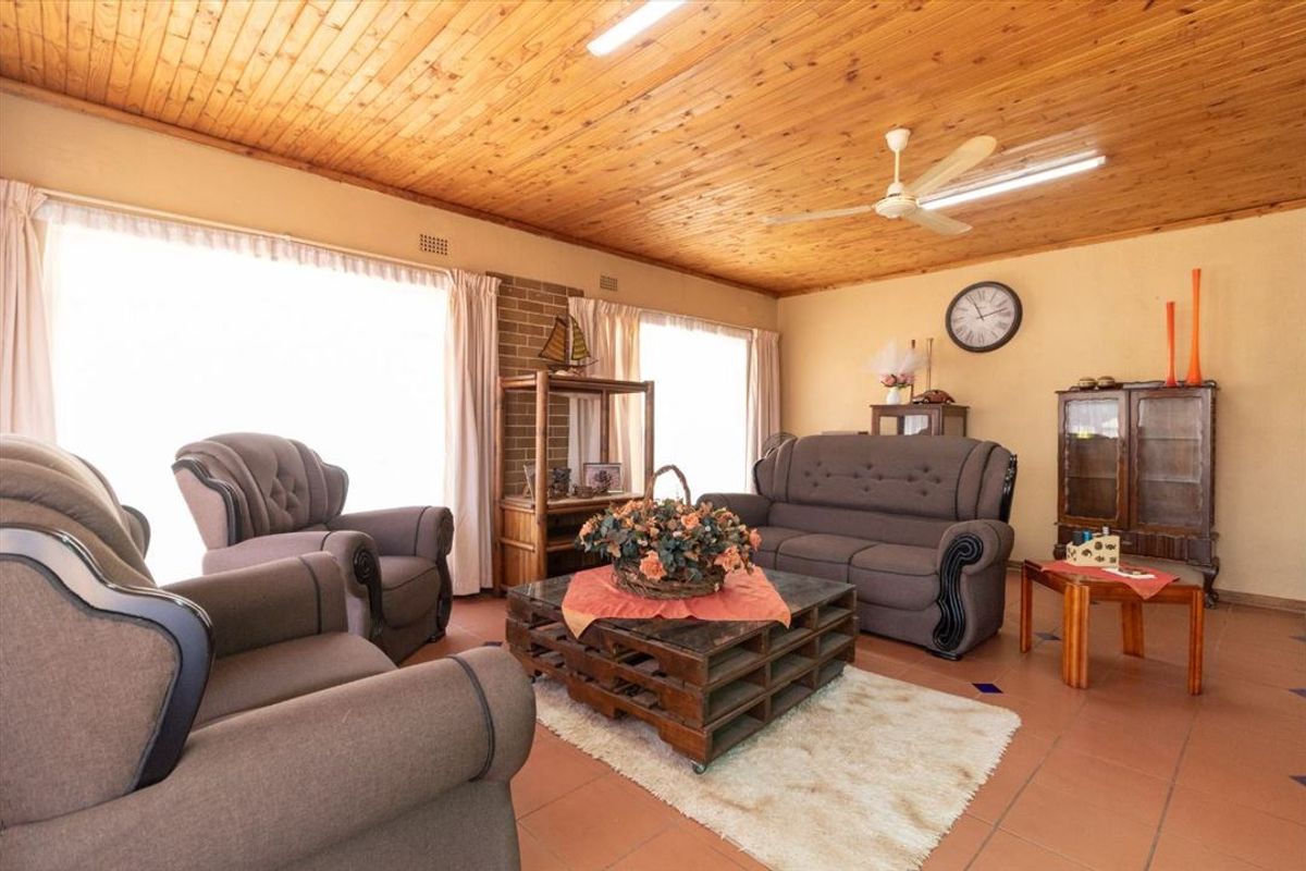 A spacious living room featuring a warm timber tongue and groove ceiling, terracotta floor tiles, and a brick feature wall.