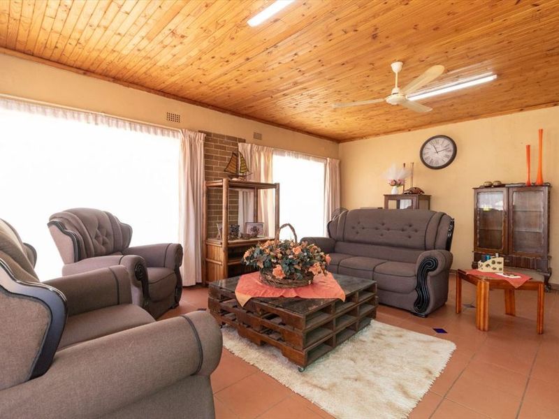 A spacious living room featuring a warm timber tongue and groove ceiling, terracotta floor tiles, and a brick feature wall.