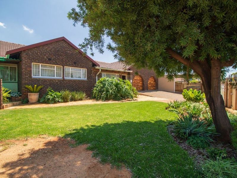 Front view of a face brick house featuring a tiled roof, arched garage doors, a paved driveway, and a well-established garden with a large tree.