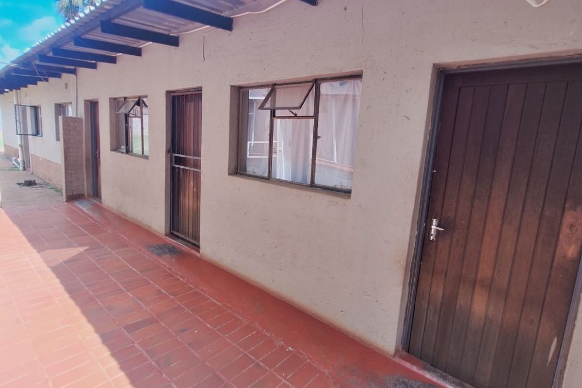 Exterior view of a rear patio area featuring tiled flooring, timber doors, and security gates along the building facade.