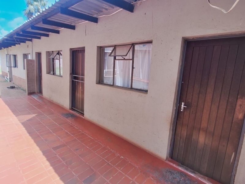 Exterior view of a rear patio area featuring tiled flooring, timber doors, and security gates along the building facade.