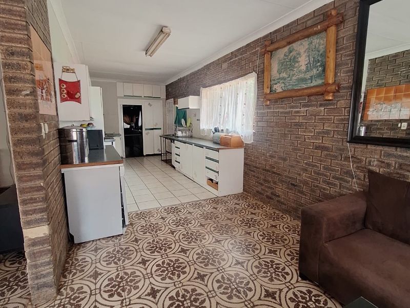 Open plan kitchen and living area featuring exposed brick walls and patterned tile flooring, offering a dated aesthetic with potential for modernization.