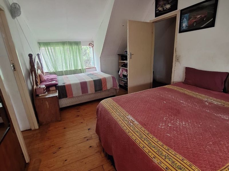 A bedroom featuring timber flooring and a sloped ceiling, offering a functional space with potential for cosmetic updates.
