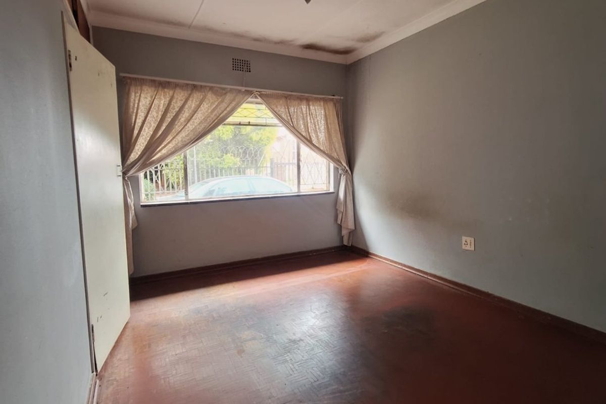An empty bedroom featuring parquet flooring and a window with natural light, requiring cosmetic updates to the walls and ceiling.