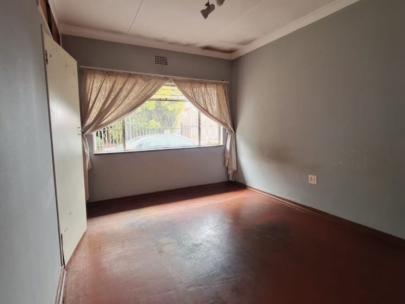 An empty bedroom featuring parquet flooring and a window with natural light, requiring cosmetic updates to the walls and ceiling.