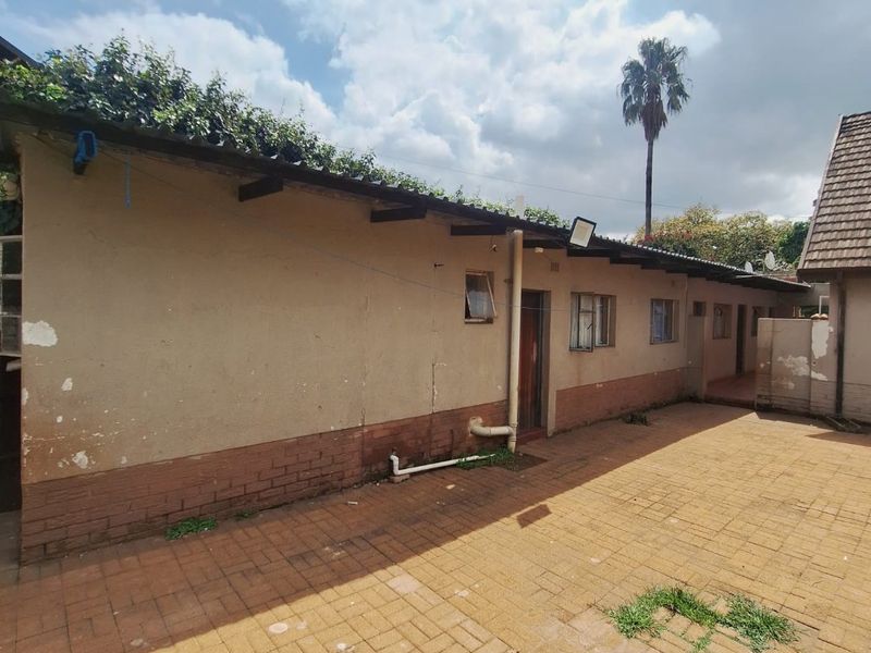 Rear exterior view of the property featuring a paved courtyard, exposed brick and plastered wall finishes, and external plumbing fixtures.