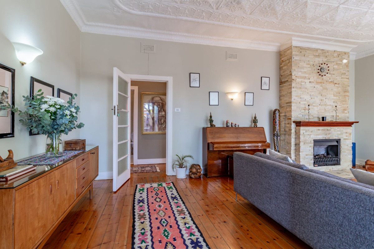 A well-maintained living room featuring polished timber flooring, an ornate ceiling, and a prominent stone fireplace as a central focal point.