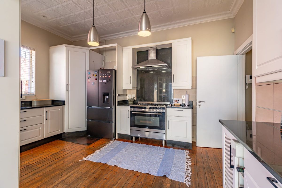 A well-maintained kitchen featuring classic white cabinetry, stone countertops, a gas stove with extractor fan, and original timber flooring under a decorative pressed ceiling.