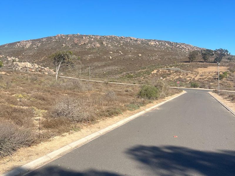 A view of a paved residential street leading towards a scenic hillside landscape.