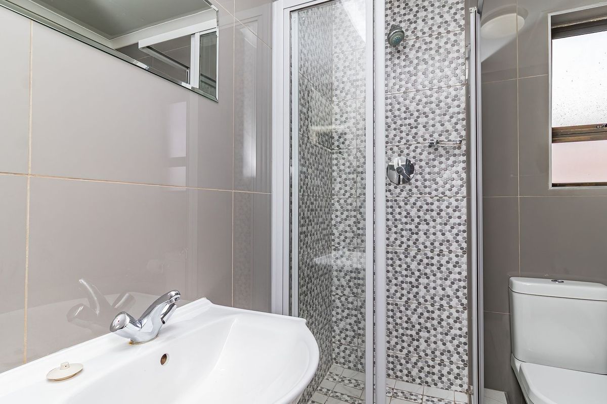 Modern bathroom featuring a glass-enclosed shower with mosaic tiling, a ceramic basin with chrome fixtures, and a clean, neutral tiled finish.
