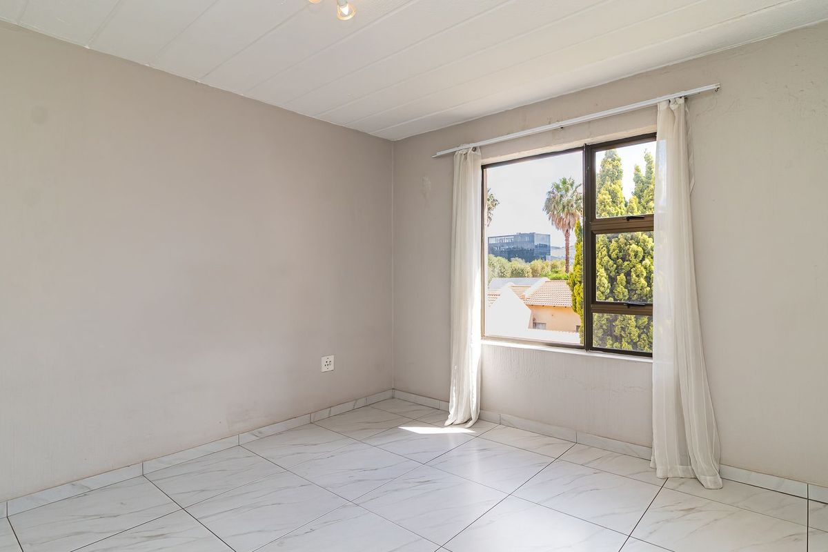 A bright, empty bedroom featuring modern marble-look floor tiles, neutral walls, and a large window providing natural light and neighborhood views.