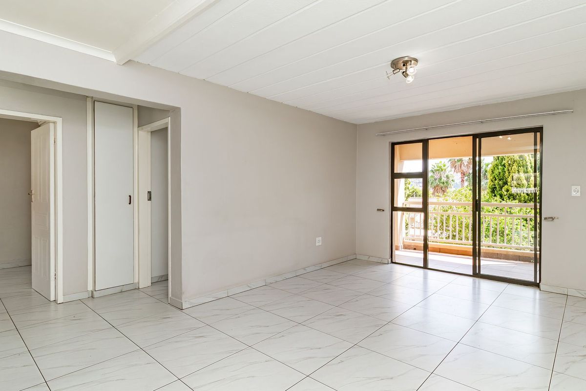 A bright, empty living room featuring neutral tiled flooring, a built-in cupboard, and sliding glass doors that open onto a balcony.