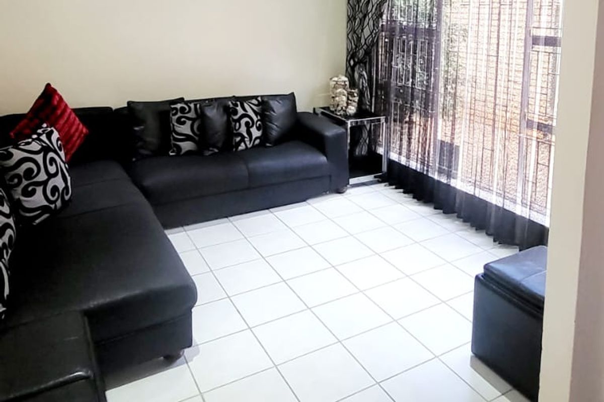 A bright living room featuring white tiled flooring, recessed downlighting, and a wall-mounted air conditioning unit with access to an outdoor area.