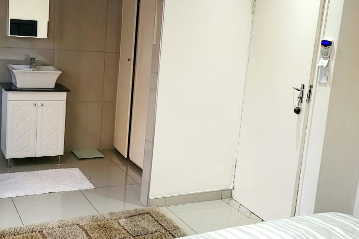 Bedroom featuring an open-plan vanity area with a basin, built-in cupboards, and tiled flooring, providing a functional and compact living space.