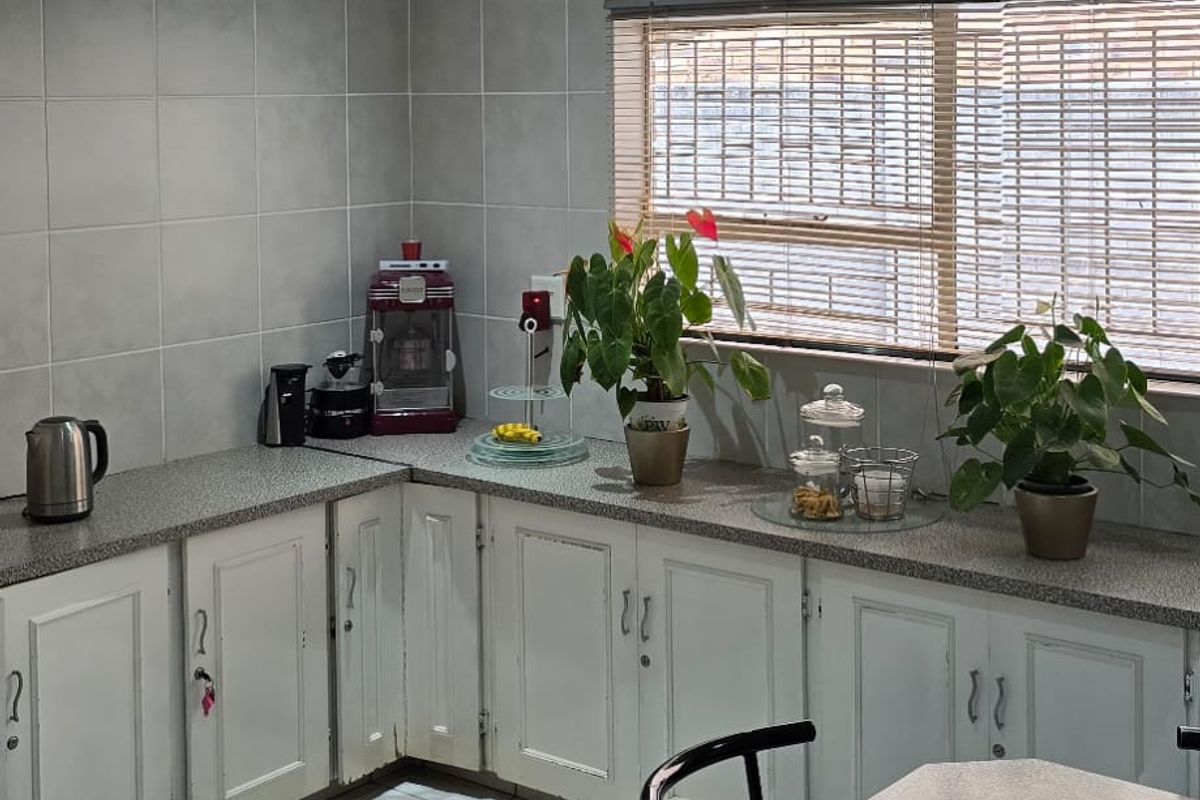 A functional kitchen featuring white cabinetry, grey tiled walls, laminate countertops, and a wall-mounted air conditioning unit.