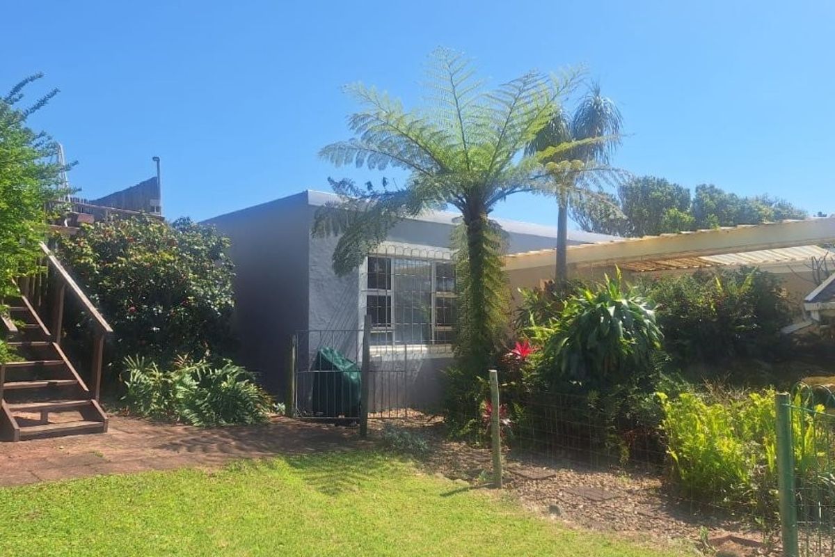 Rear exterior view featuring a paved patio, timber staircase, and metal pergola set within a landscaped garden area.