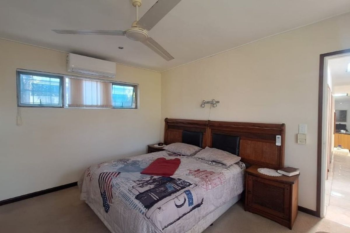 A functional bedroom featuring a ceiling fan, split system air conditioning, and awning windows, with direct access to a tiled hallway.