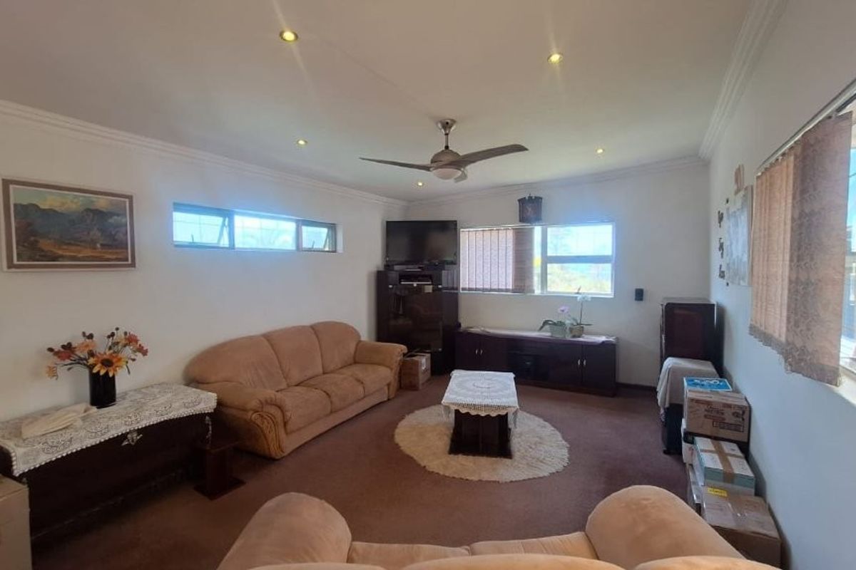 A spacious living room featuring recessed downlighting, a ceiling fan, and large windows with security bars, offering a functional and well-lit living space.
