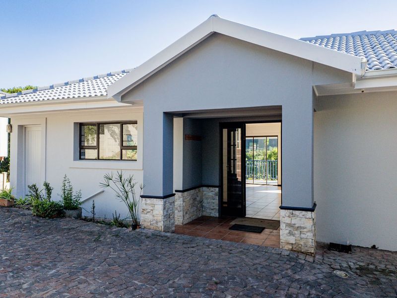 Front facade of the house featuring a covered entrance, stone cladding accents, tiled roof, and a paved driveway.