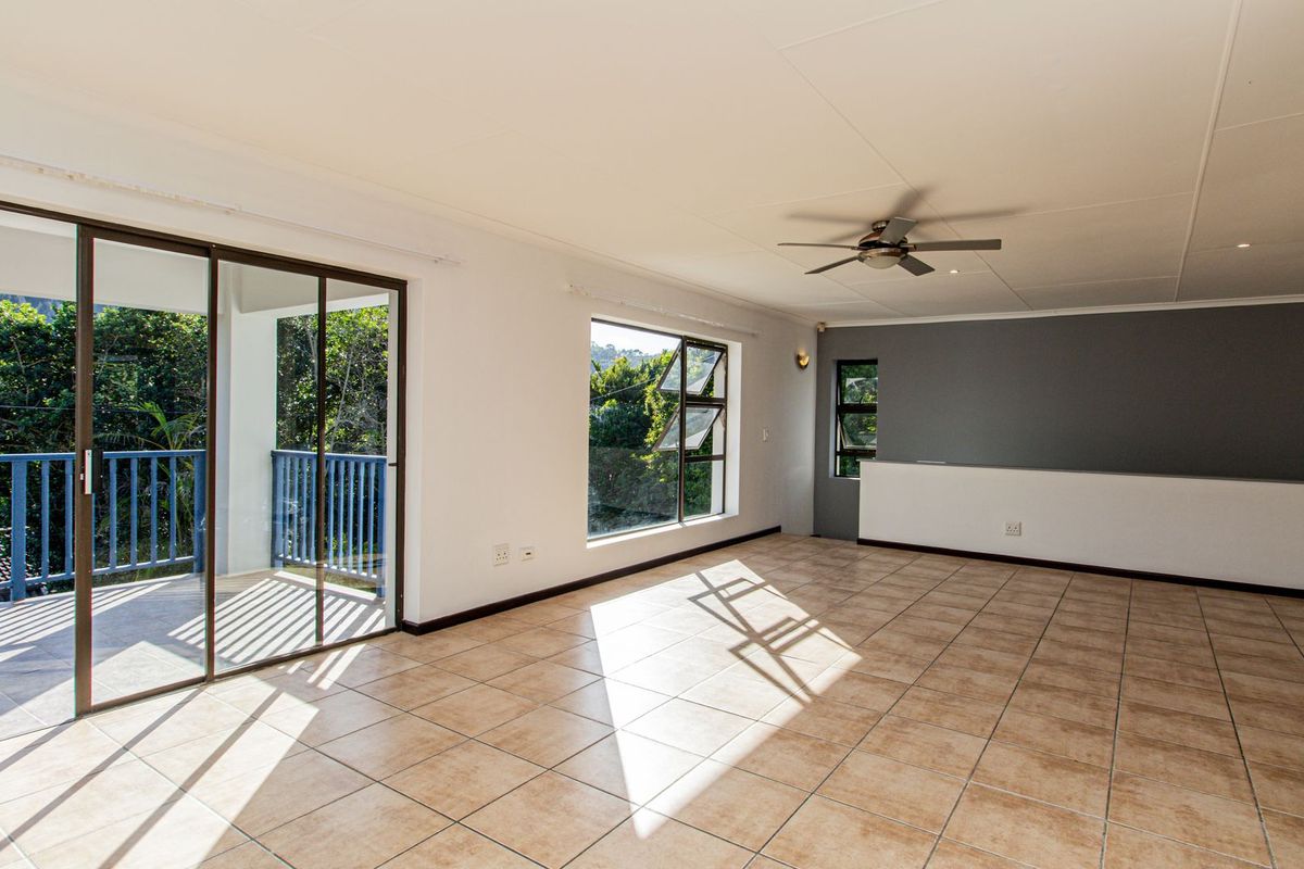 Spacious, light-filled living area featuring neutral tiled flooring, a ceiling fan, and large sliding doors opening onto a private balcony with scenic views.