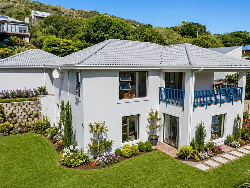 A well-maintained two-story residential property featuring a tiled roof, a private balcony, and a beautifully landscaped garden with stone stairs and paved pathways.