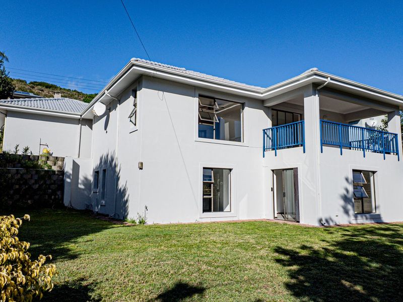 Rear view of a two-story residential house featuring a balcony with blue railings, large windows, and a well-maintained lawn.
