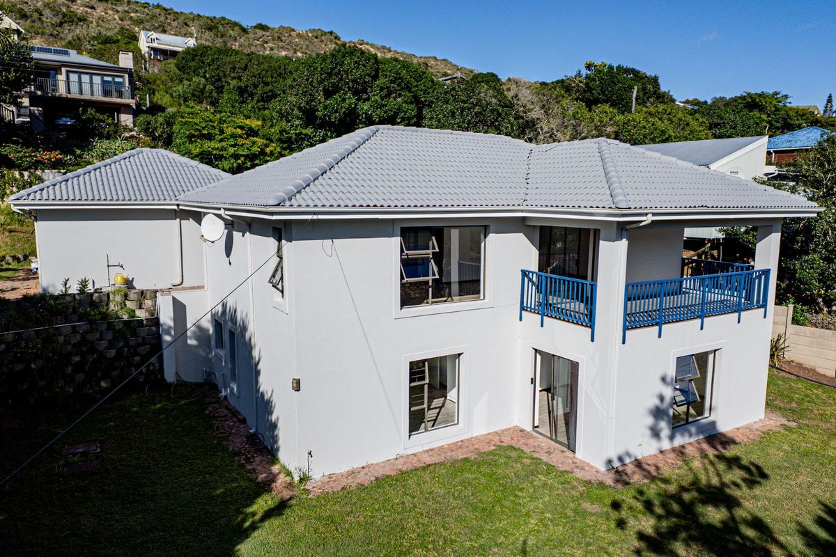 Rear view of a two-story house featuring a tiled roof, a balcony with blue railings, and a landscaped garden area.