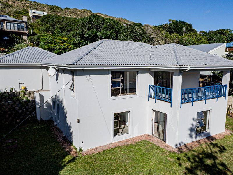 Rear view of a two-story house featuring a tiled roof, a balcony with blue railings, and a landscaped garden area.
