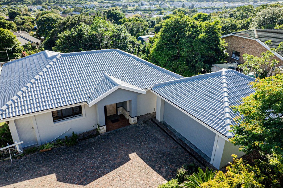 Aerial view of a well-maintained residential property featuring a tiled roof, paved driveway, and double garage set within a lush, green neighborhood.