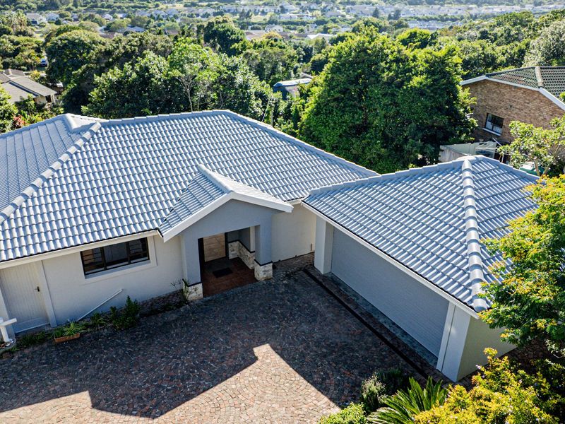 Aerial view of a well-maintained residential property featuring a tiled roof, paved driveway, and double garage set within a lush, green neighborhood.
