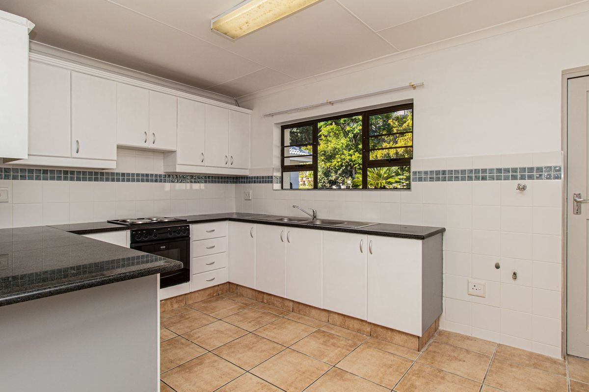 A functional kitchen featuring white cabinetry, granite countertops, built-in oven and hob, and tiled flooring with a window overlooking the garden.