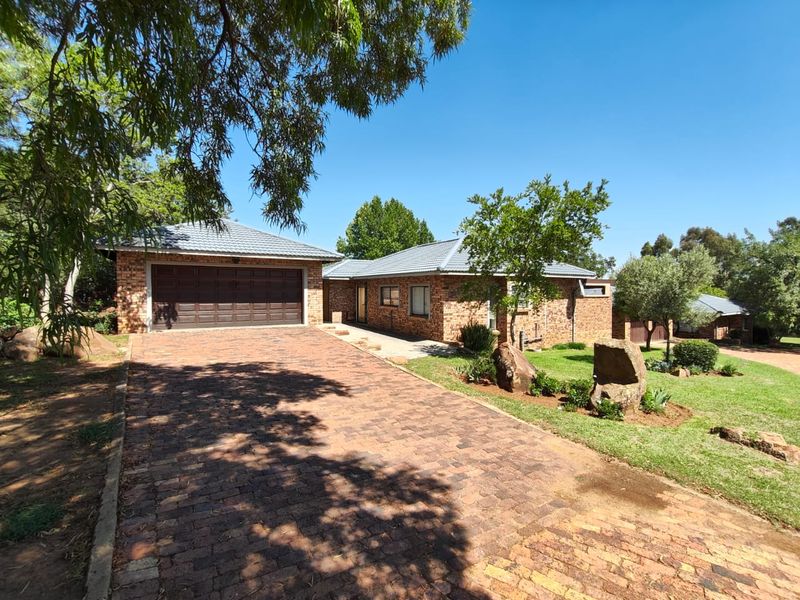 A well-maintained single-story brick house featuring a paved driveway, double garage, and established garden surroundings.