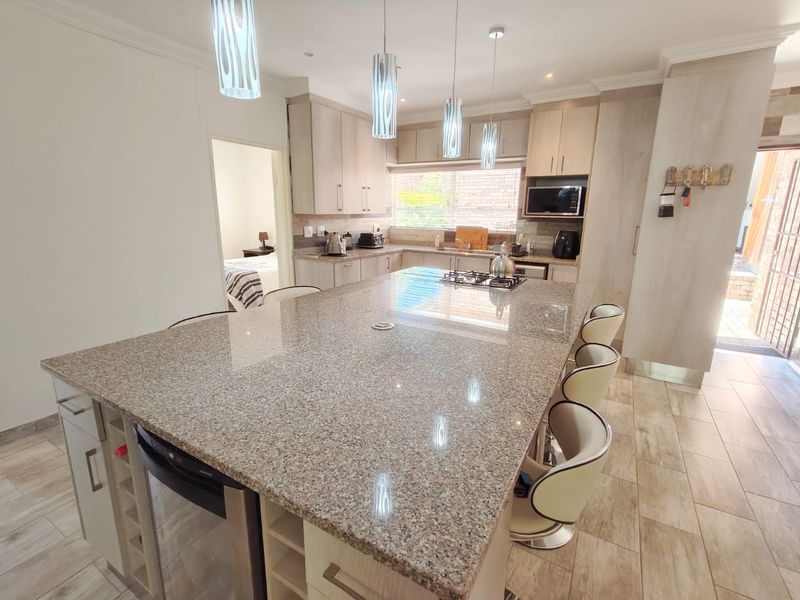 Modern kitchen featuring a large granite-topped island, ample built-in cabinetry, integrated appliances, and stylish pendant lighting, creating a functional and contemporary cooking space.