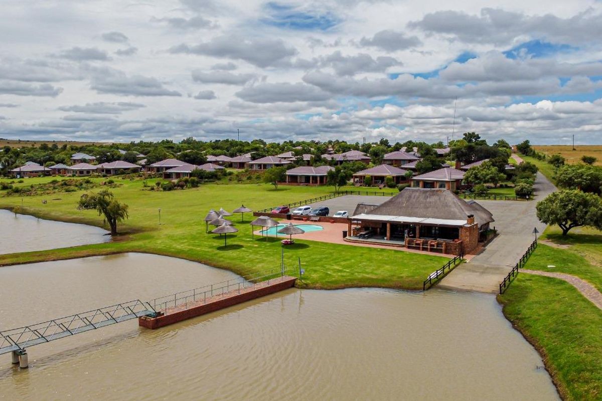 Aerial view of a residential estate featuring a clubhouse, swimming pool, and a pedestrian bridge over a lake.