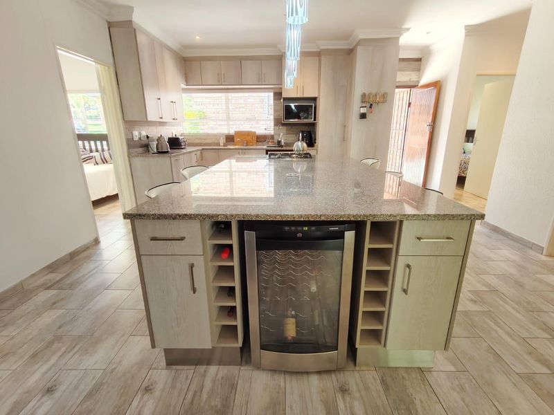 Modern kitchen featuring a large granite-topped island with integrated wine cooler, ample cabinetry, and built-in appliances, finished with contemporary tiled flooring.