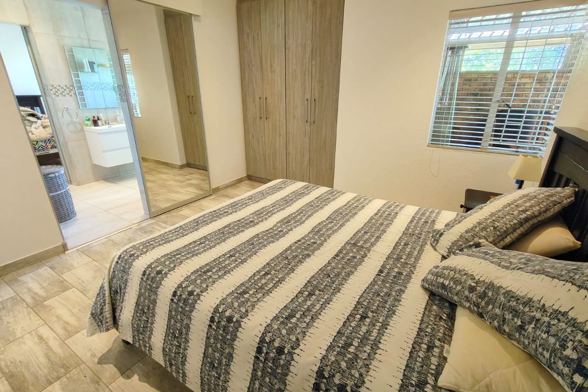 A well-maintained bedroom featuring built-in cupboards, tiled flooring, and an adjoining en-suite bathroom with modern fixtures.